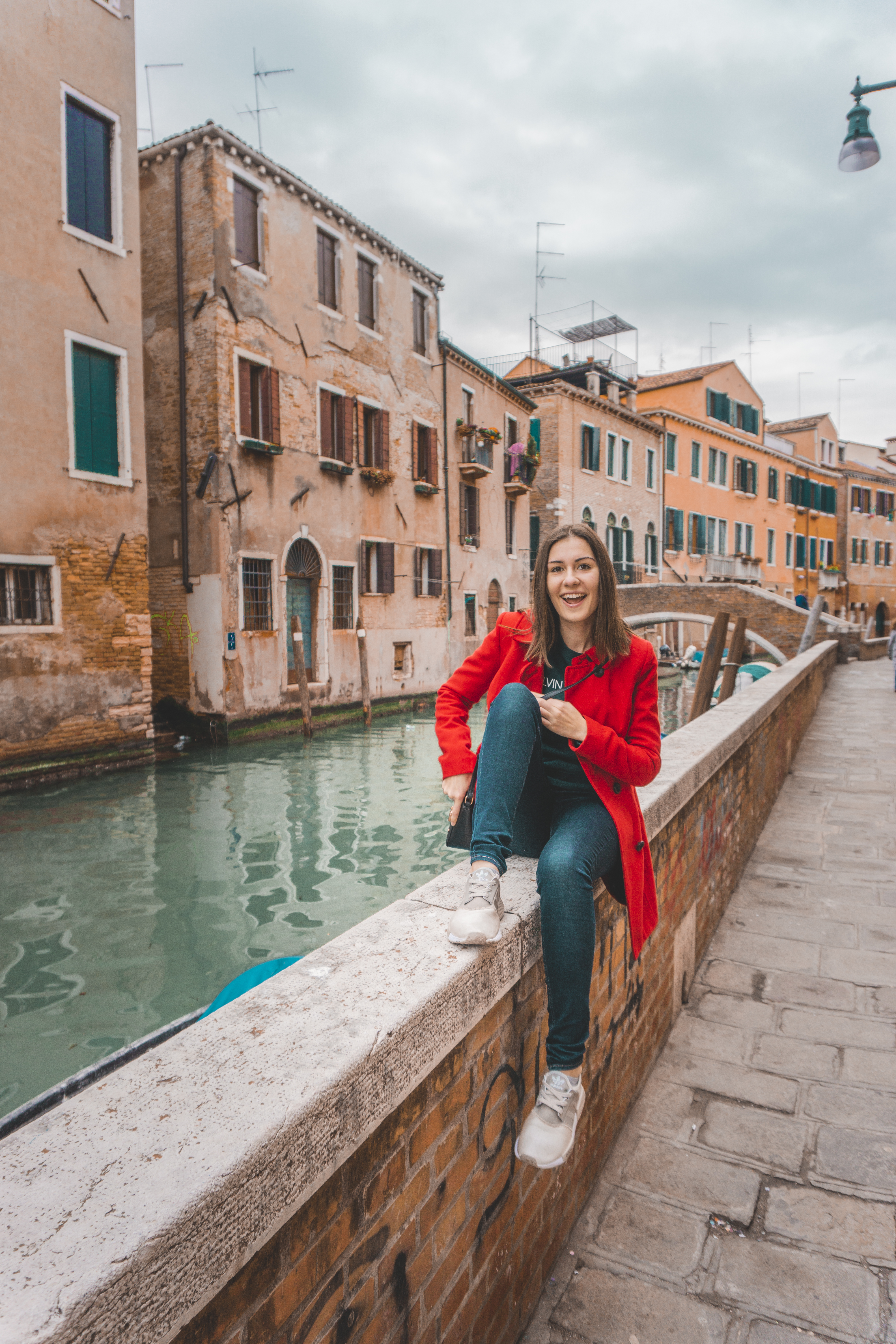 A girl in the red coat sitting in Venice, Italy and smiling. 