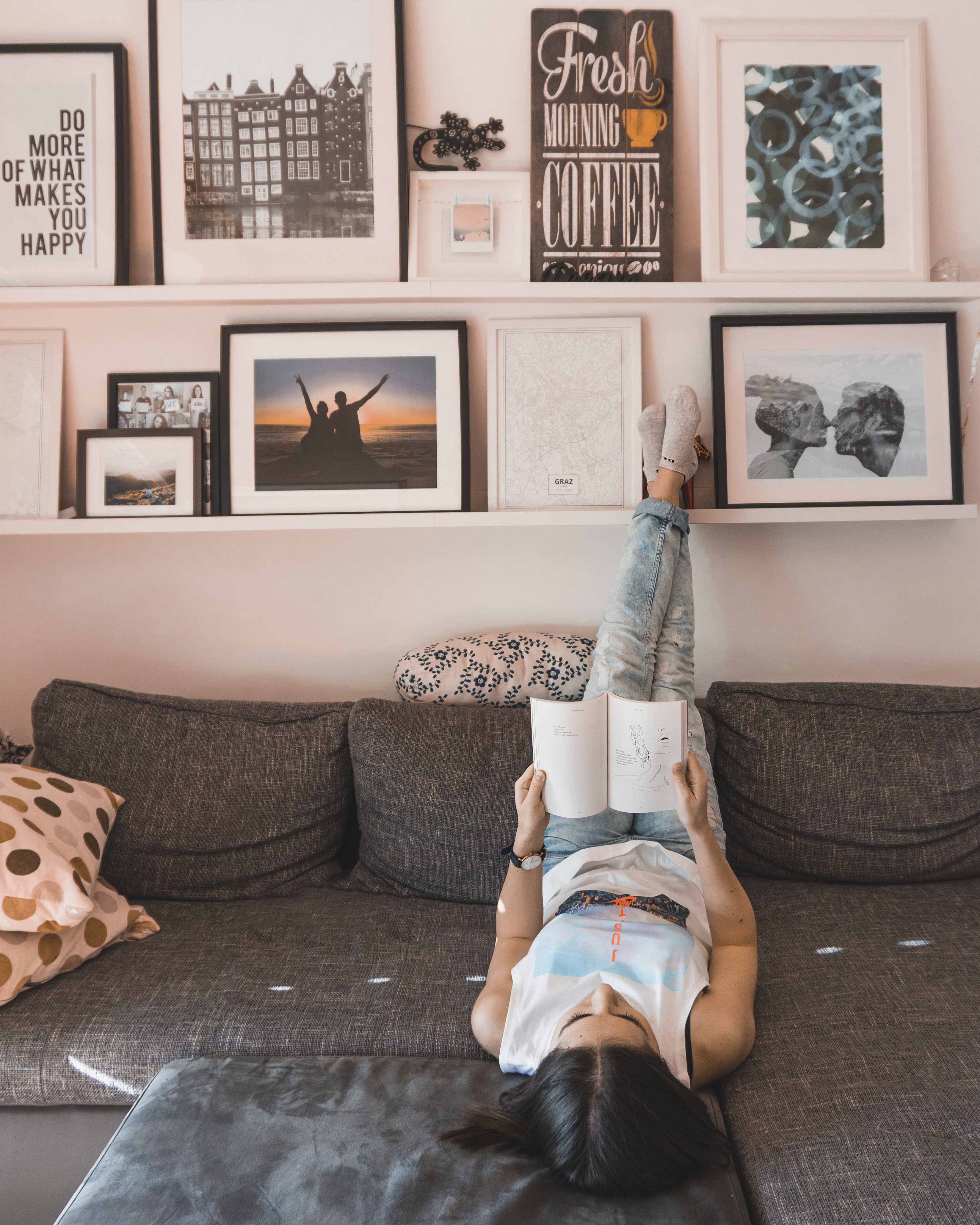 A girl reading book upside down. Behind there's a wall full of art and posters