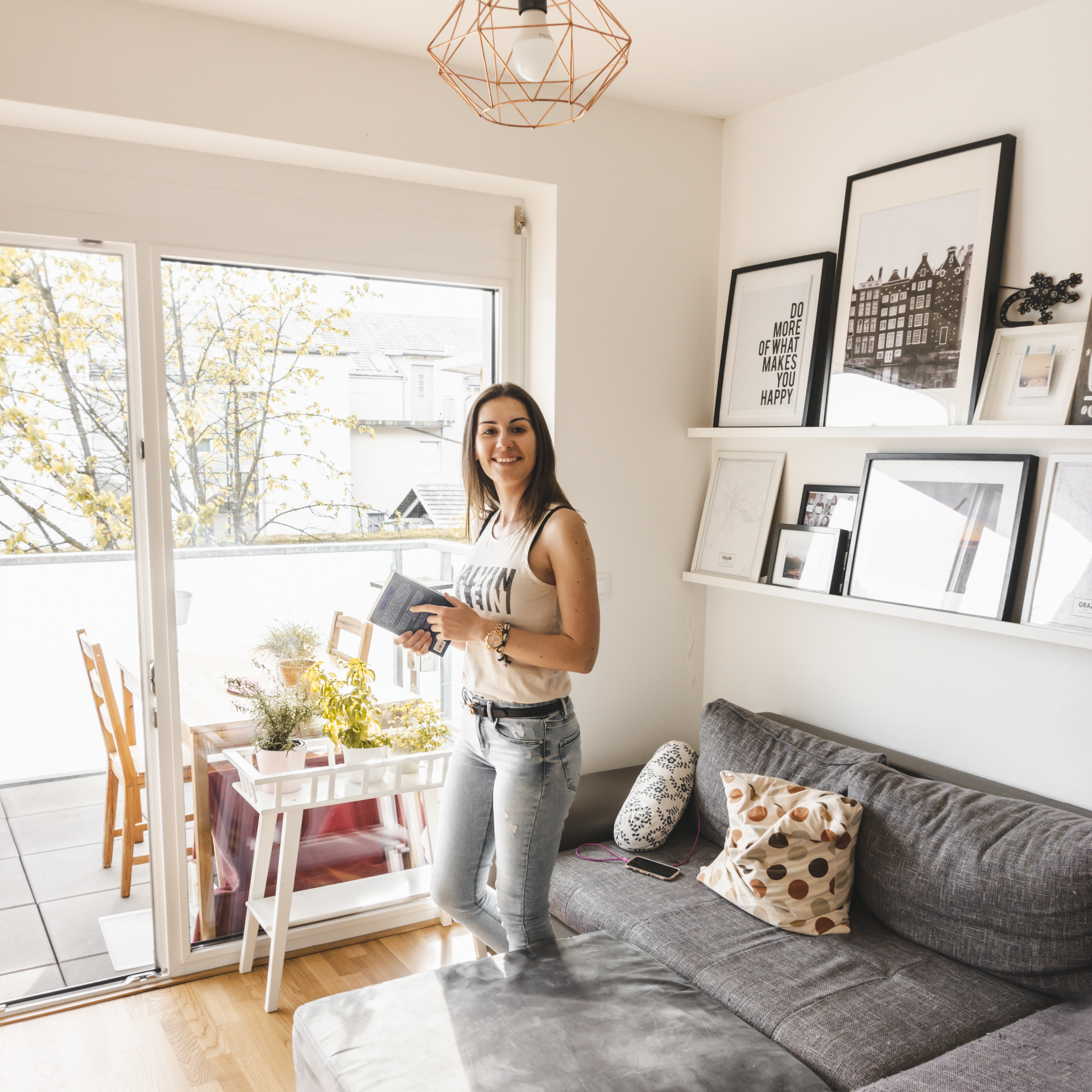 A girl holding a book and standing in the Scandinavian decored room with a big balcony window.
