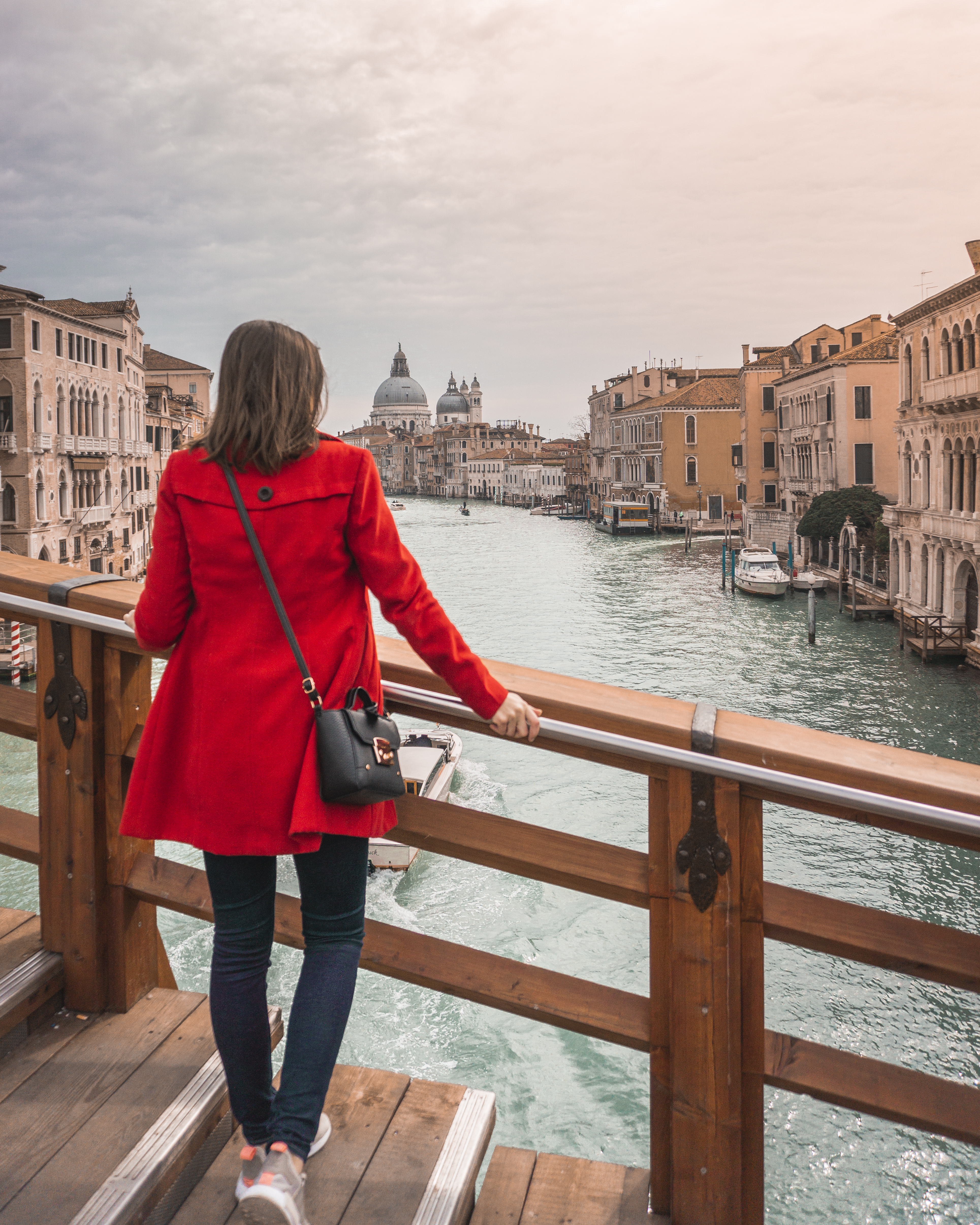 A girl in the red coat standing with the back to the photographer and looking at the Grand Canal in Venice. 