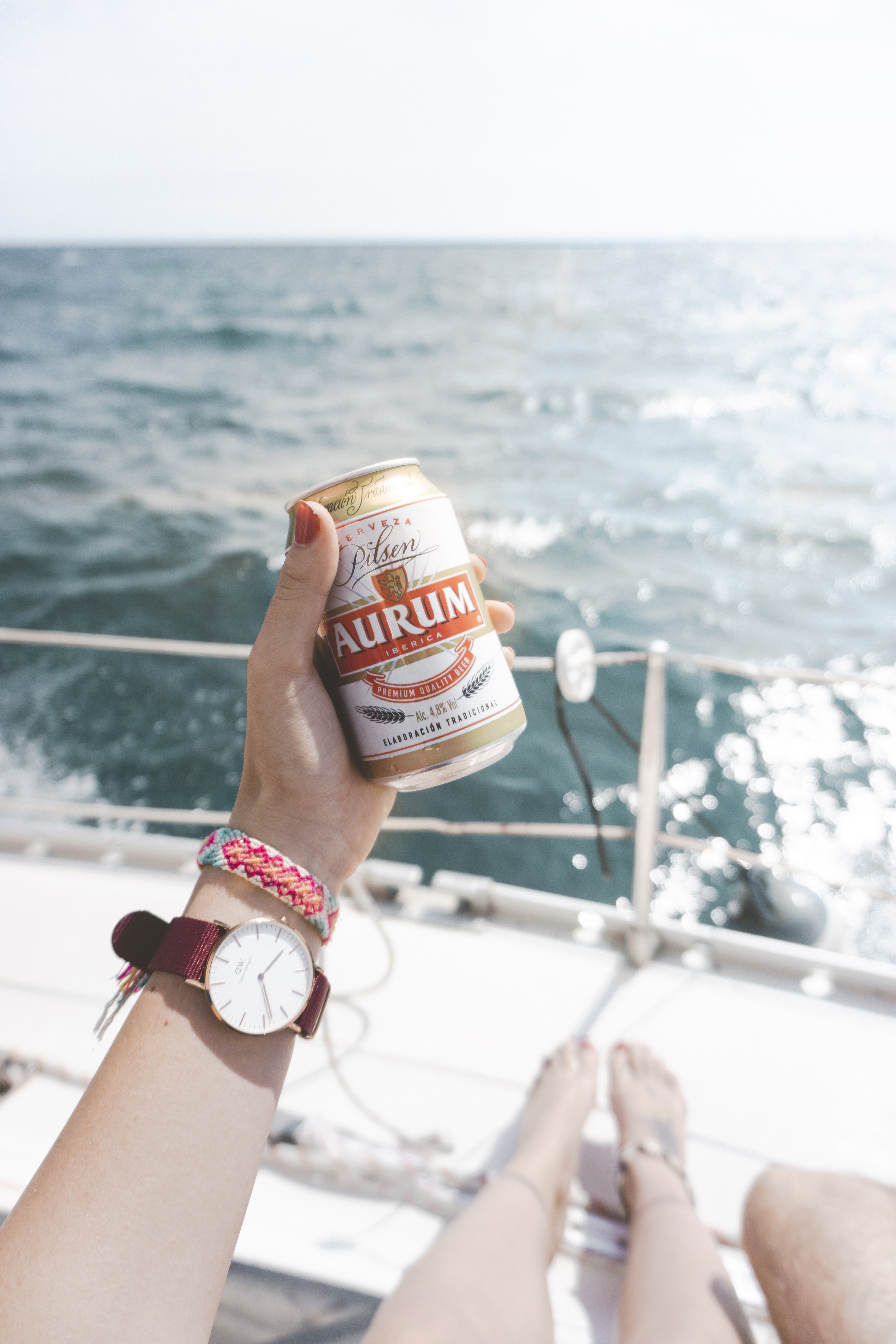 A girl holding a beer can in her hand, with the watch on her wrist, sitting on the boat. 